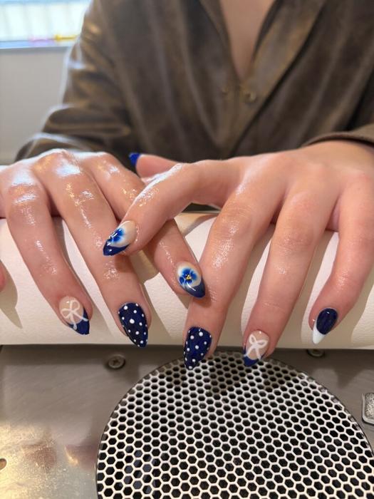 Navy almond nails mixing white polka dots, hand-painted bows, and blue flower accents