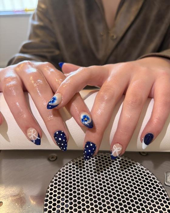 Navy almond nails mixing white polka dots, hand-painted bows, and blue flower accents