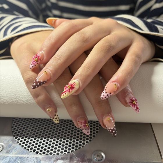 Long stiletto nails with dotted brown french tips, pink painted lilies, and gold gems